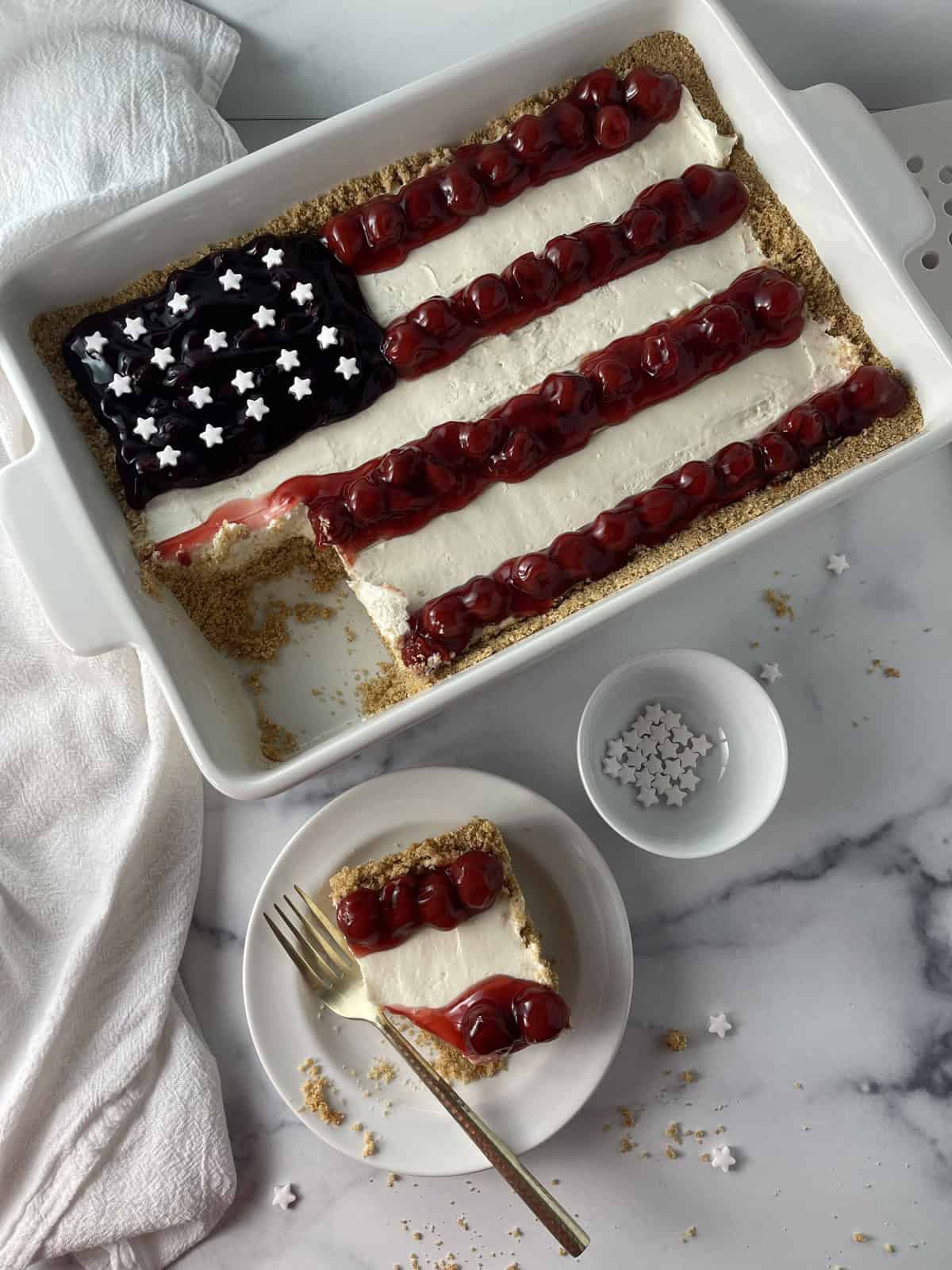 American flag cheesecake in white 13x9 dish with slice taken out onto plate.