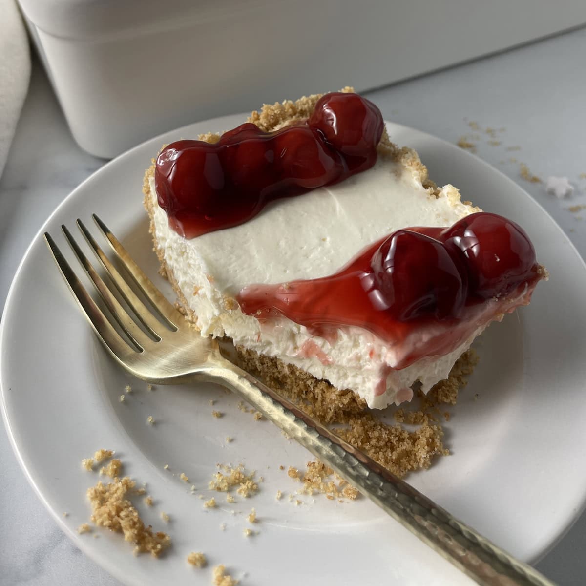 Slice of no bake cheesecake on white plate with cherries on top.