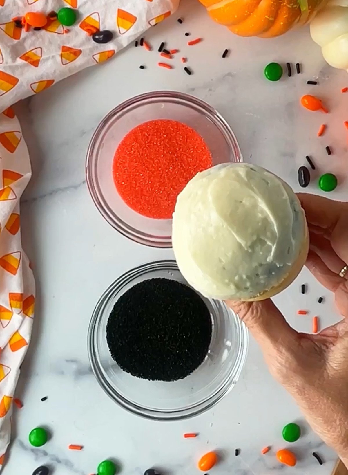 Dipping cupcake in orange and black sprinkles.