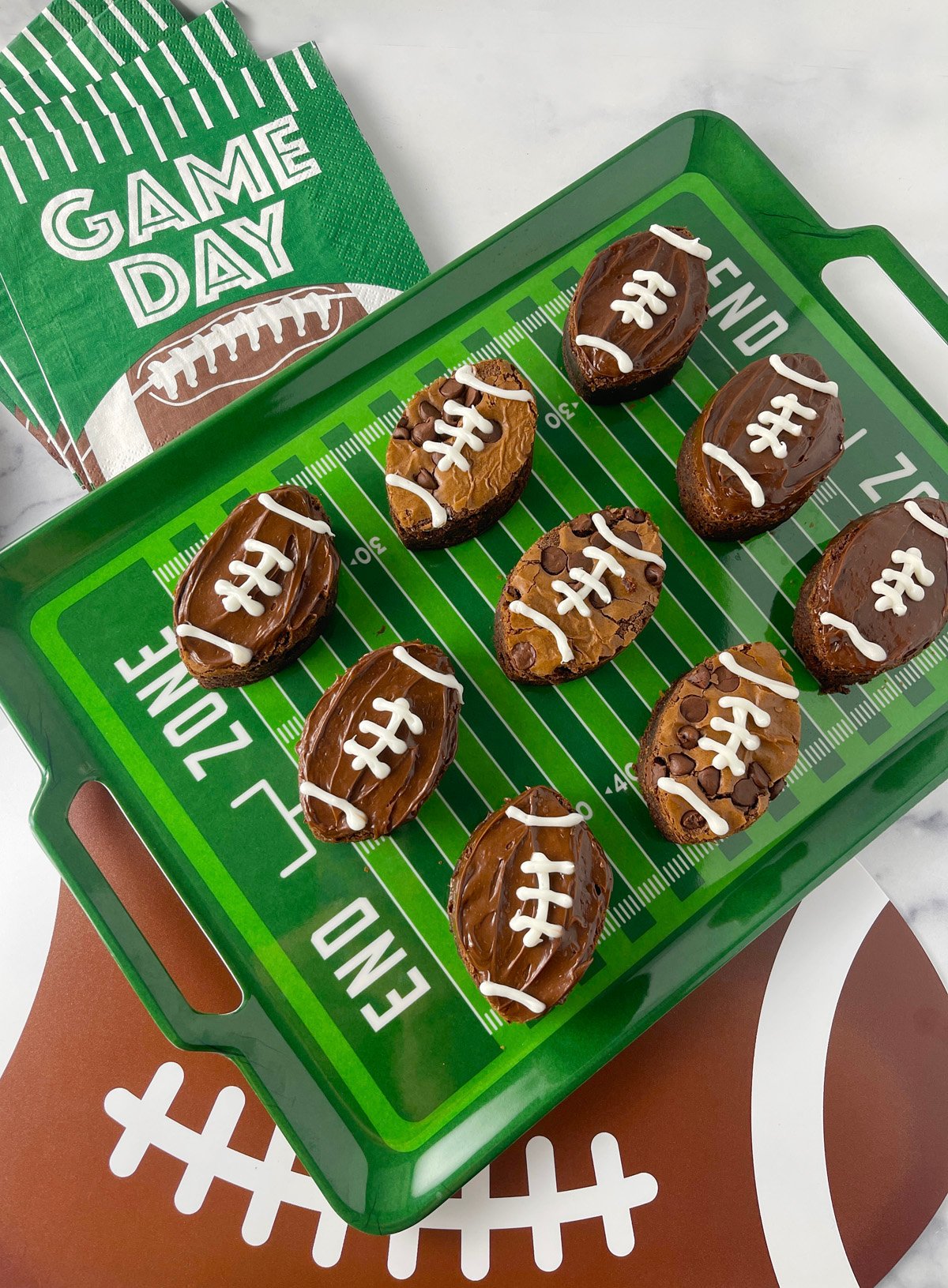 Football shaped chocolate frosted brownies on a green football field tray.