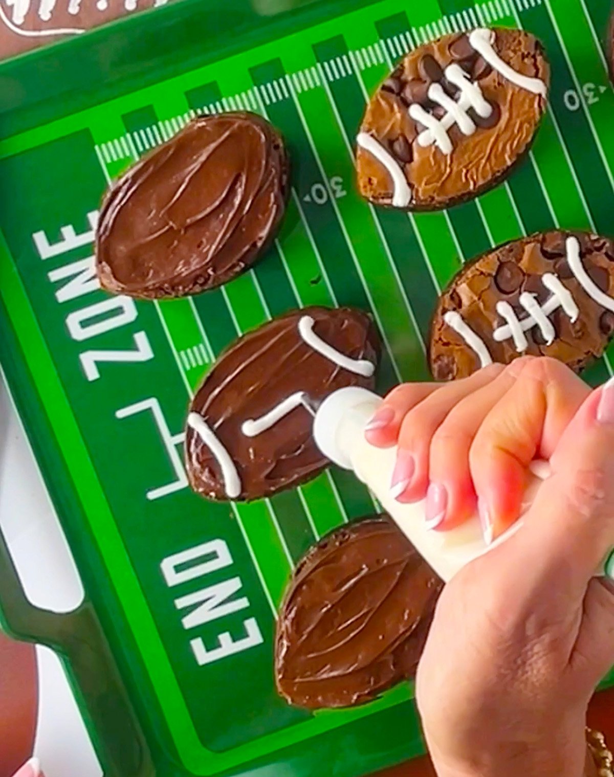 Piping football laces on brownies with white icing in a pastry bag.