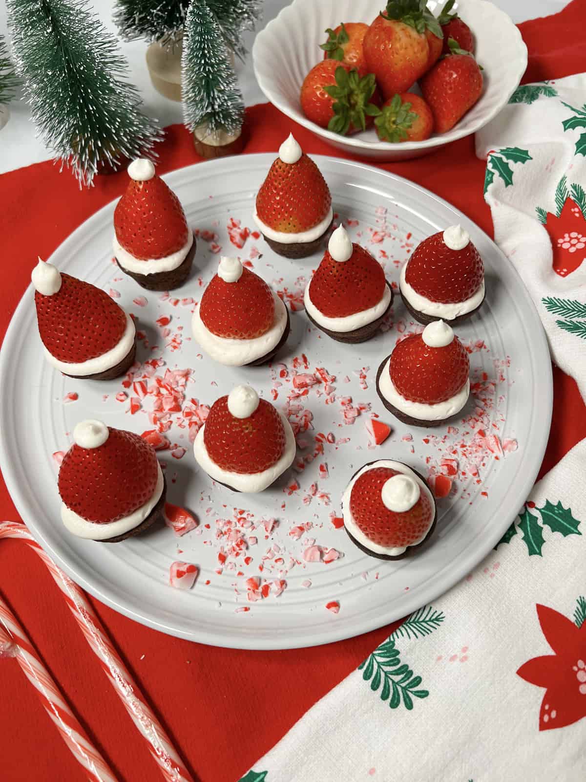 A white plate full of strawberries decorated like Santa hats on brownies.