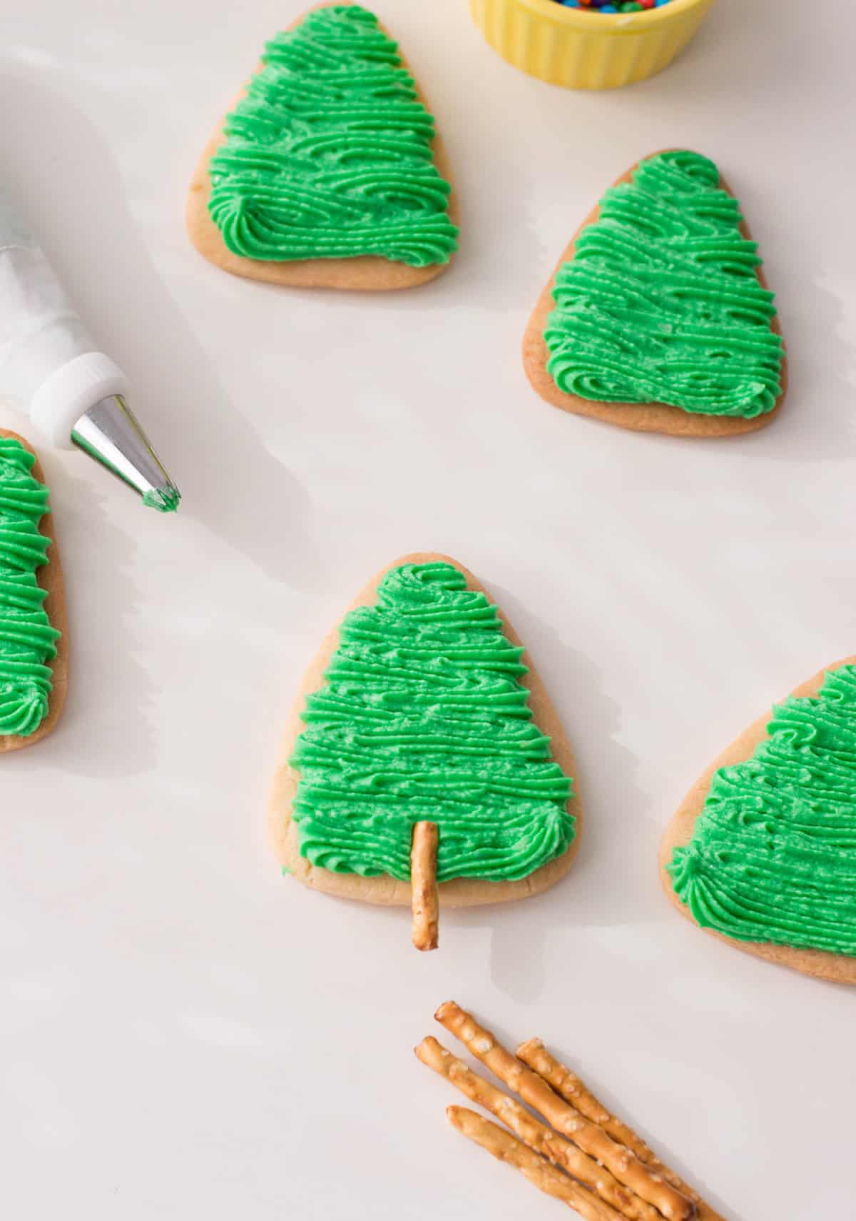 Piping green frosting on top of Christmas tree sugar cookies.